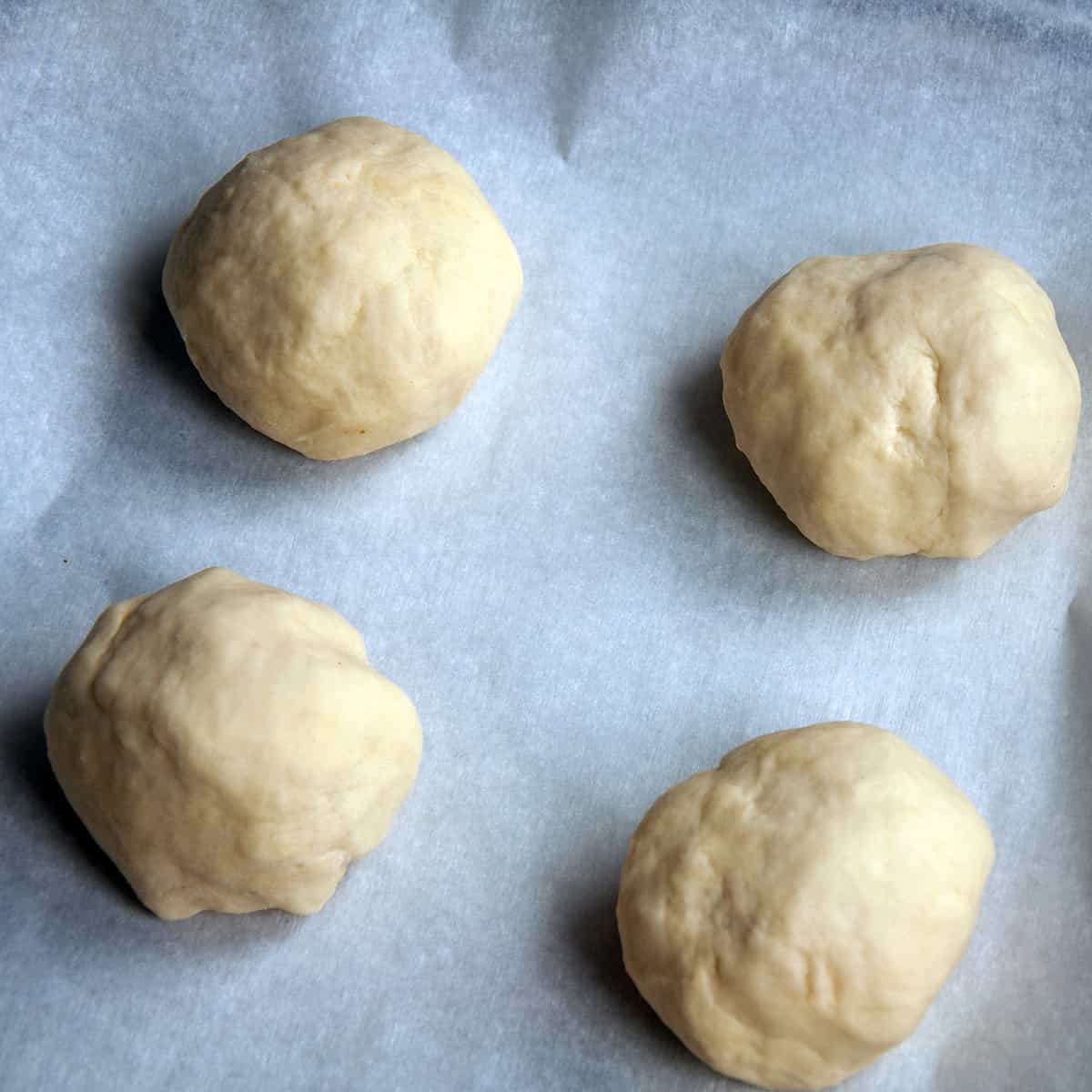 Four dough balls on a piece of parchment paper.