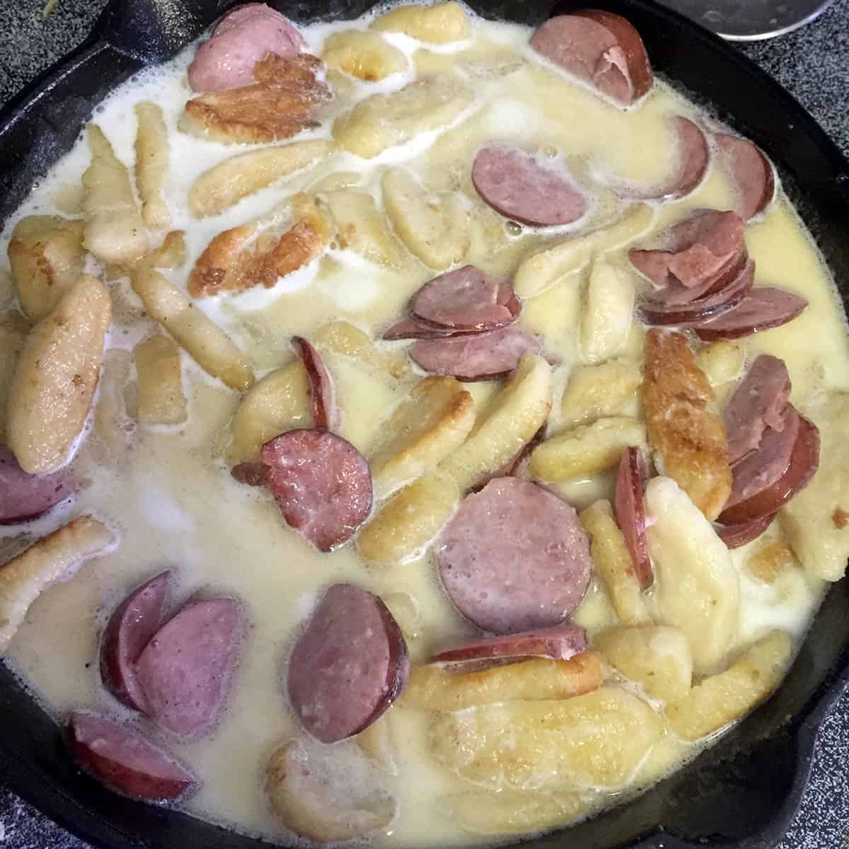 A skillet of sausage knoephla mix being brought to a simmer.