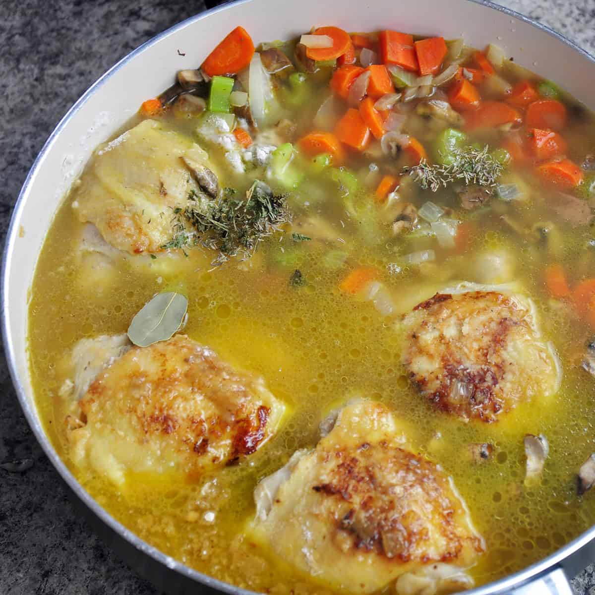 Chicken thighs in chicken stock, herbs, and vegetables.