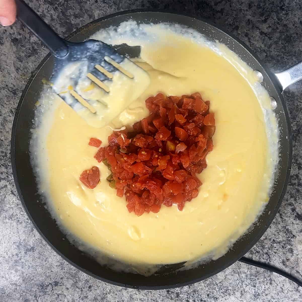 Rotel and Cheese A person stirring a pan with cheese and tomatoes.