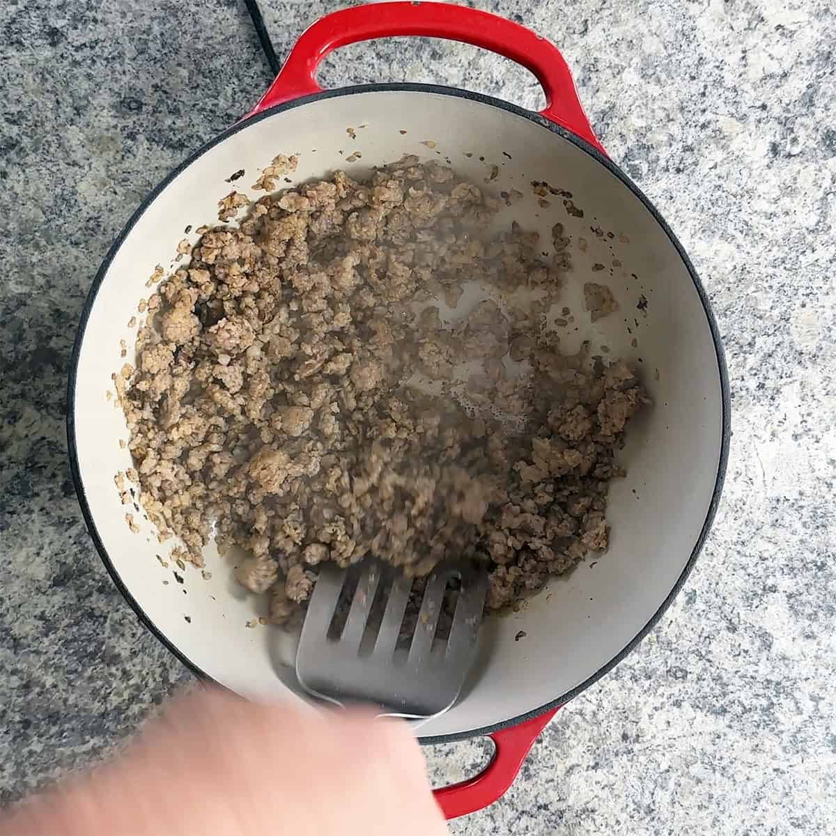Stirring Italian sausage in a dutch oven.